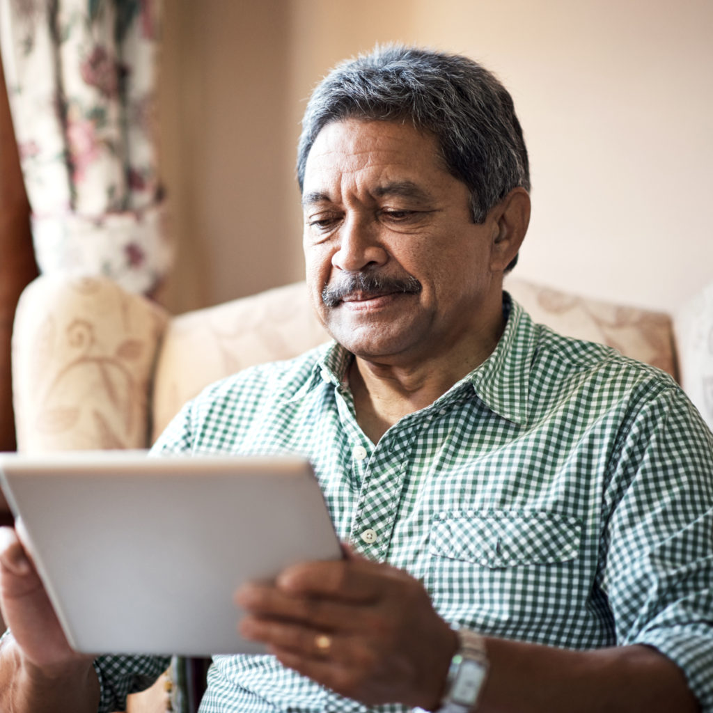Senior man using his digital tablet while relaxing at home